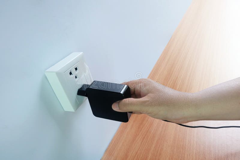 La mano del ` s de los hombres tiene enchufes, adaptadores, enchufes del cable eléctrico, dispositivos en piso de madera foto de archivo libre de regalías La mano del ` s de los hombres tiene enchufes, adaptadores, enchufes del cable eléctrico, dispositivos en piso de madera foto de archivo libre de regalías