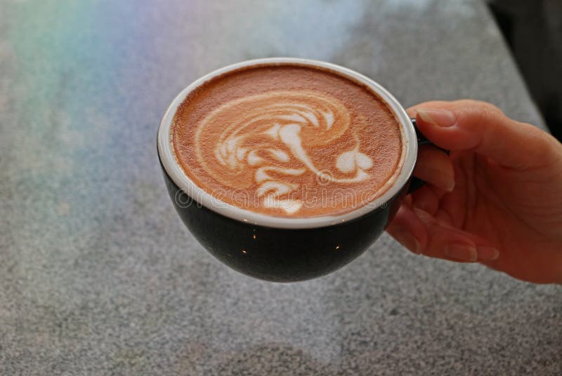 La mano della donna che tiene una tazza del caff? del cappuccino con la tavola di pietra confusa nel contesto fotografia stock La mano della donna che tiene una tazza del caff? del cappuccino con la tavola di pietra confusa nel contesto fotografia stock
