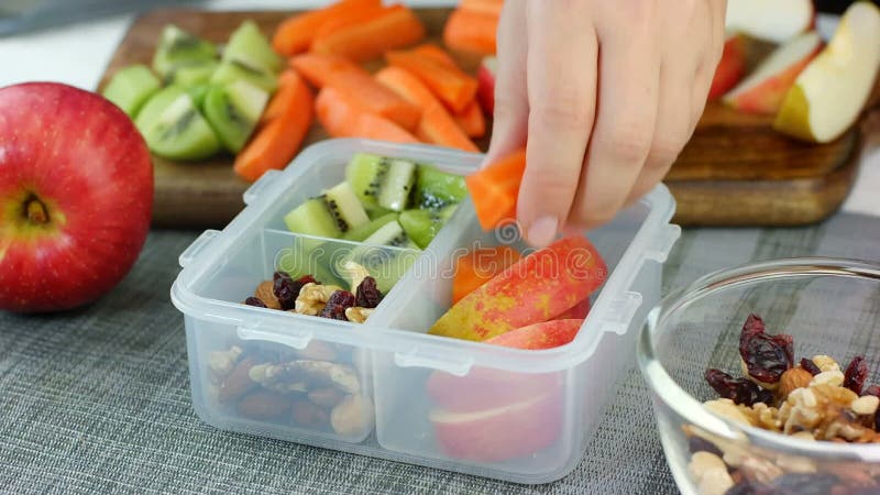 La mano della donna ha messo la frutta sana ed il dado fa un spuntino nella scatola di pranzo