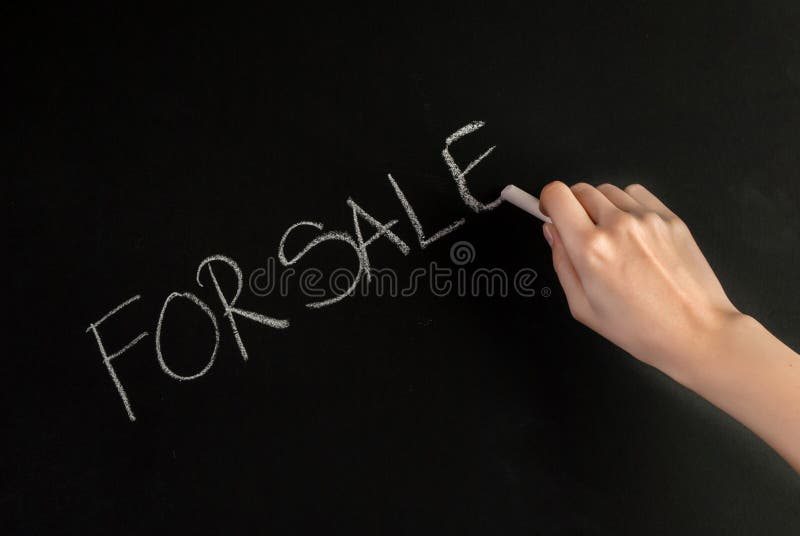 La mano della donna scrive la parola da vendere sulla lavagna con gesso bianco immagini stock La mano della donna scrive la parola da vendere sulla lavagna con gesso bianco immagini stock