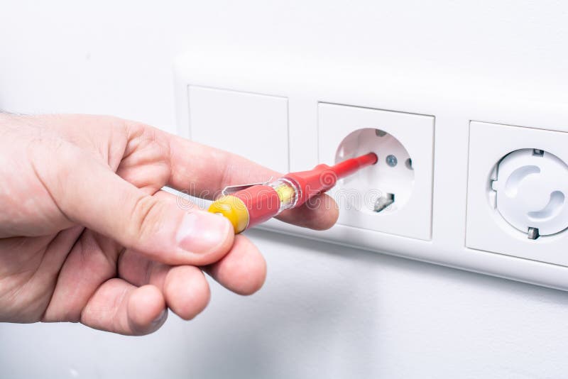 La mano di un elettricista Holding un tester di fase in una presa a muro, la luce d'ardore indica una corrente attiva immagini stock La mano di un elettricista Holding un tester di fase in una presa a muro, la luce d'ardore indica una corrente attiva immagini stock