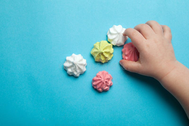 La mano di un piccolo bambino prende il dolce festivo francese della meringa su un fondo blu fotografia stock libera da diritti La mano di un piccolo bambino prende il dolce festivo francese della meringa su un fondo blu fotografia stock libera da diritti