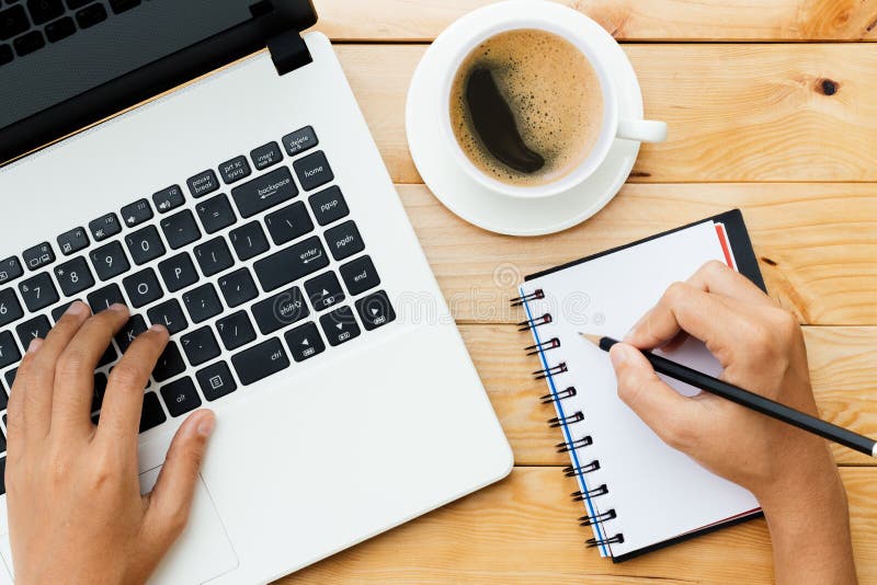 La mano facendo uso del computer portatile e scrive la nota ispira l'idea su legno immagini stock libere da diritti La mano facendo uso del computer portatile e scrive la nota ispira l'idea su legno immagini stock libere da diritti