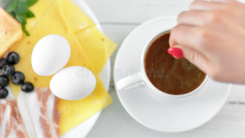 La mano femenina que tomaba la leche de mezcla de la cuchara metálica en el primer POV de la taza de café tiró la visión desde ar