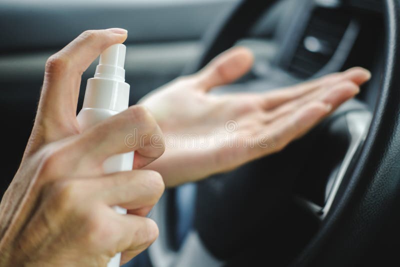 La mano maschile con spray disinfettante disinfetta la superficie della mano in un'auto Covid-19 Pandemia di quarantena del Coron