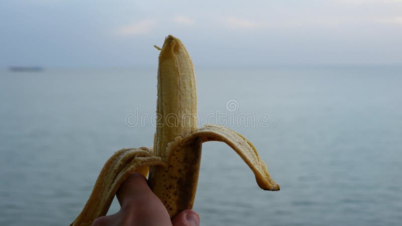 La mano maschile tiene una banana sbucciata al di sopra del livello del mare su un mare di navi da crociera sullo sfondo