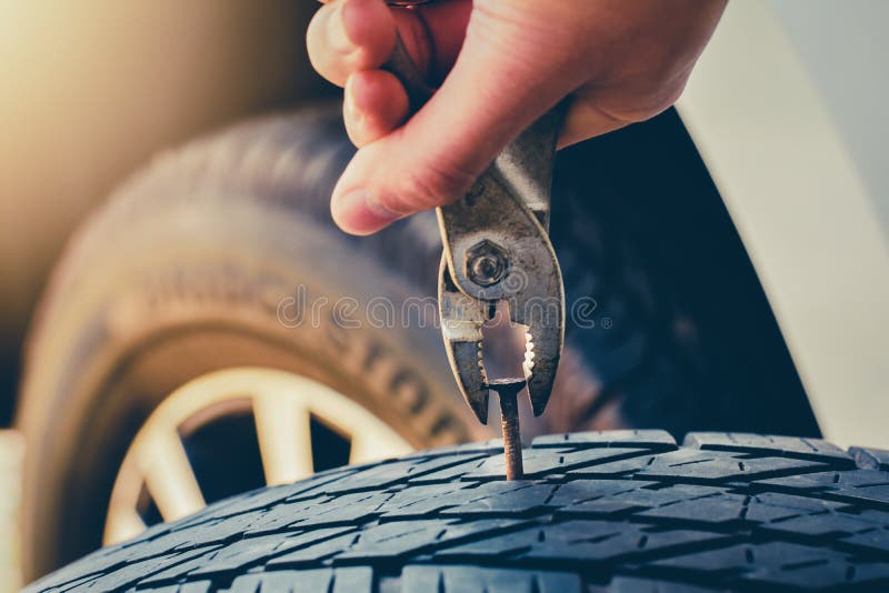 La mano que tira para quitar un clavo en el neumático, fijación del neumático desinflado y repara el neumático se está escapando