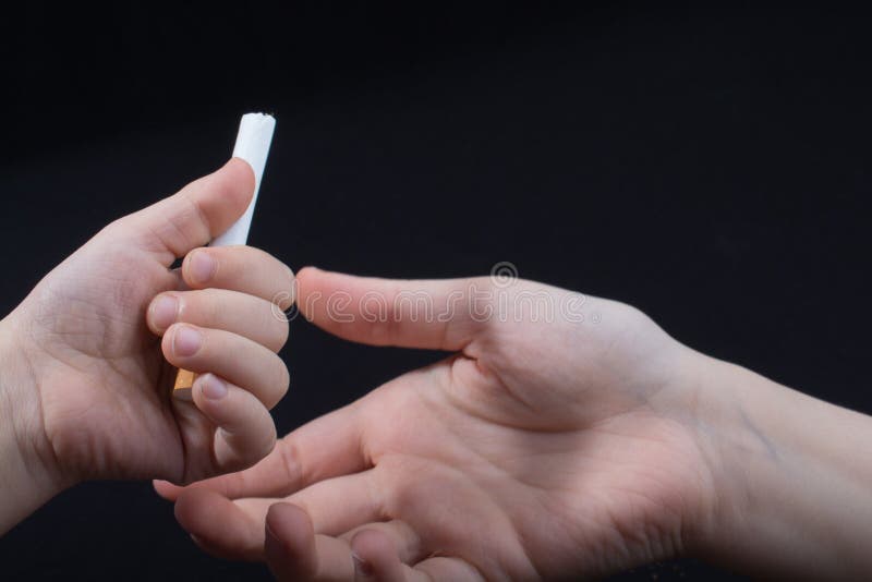 La mano sta cedendo la sigaretta su fondo nero fotografia stock La mano sta cedendo la sigaretta su fondo nero fotografia stock