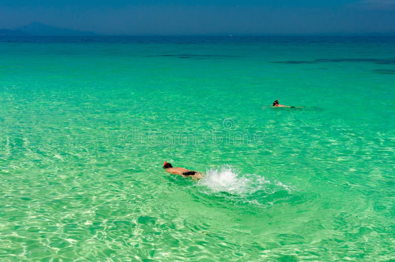 La mer clair comme de l'eau de roche de turquoise avec l'homme font presque naviguer au schnorchel dans l'eau photos stock La mer clair comme de l'eau de roche de turquoise avec l'homme font presque naviguer au schnorchel dans l'eau photos stock