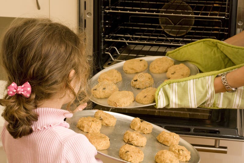 La momia de ayuda de la muchacha cuece al horno las galletas en horno