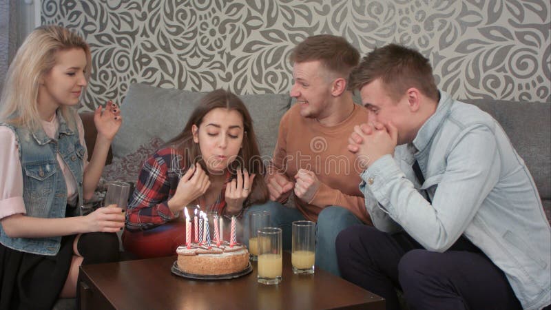 La muchacha adolescente atractiva celebra su cumpleaños con los amigos en casa y sopla hacia fuera las velas en la torta y bebe l foto de archivo La muchacha adolescente atractiva celebra su cumpleaños con los amigos en casa y sopla hacia fuera las velas en la torta y bebe l foto de archivo