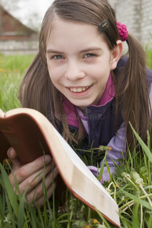 Teen girl reads book laying on grass. Teen girl reads book laying on grass