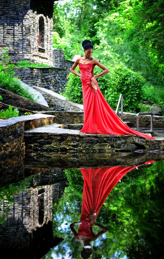 La Muchacha Afroamericana En Un Vestido Rojo Con Los Zapatos Rojos a Disposición Vale En El Verano En Agua Las Piedras E Foto de archivo - Imagen de cubo,