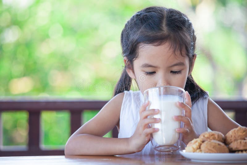 La muchacha asiática linda del pequeño niño está bebiendo una leche del vidrio imagen de archivo