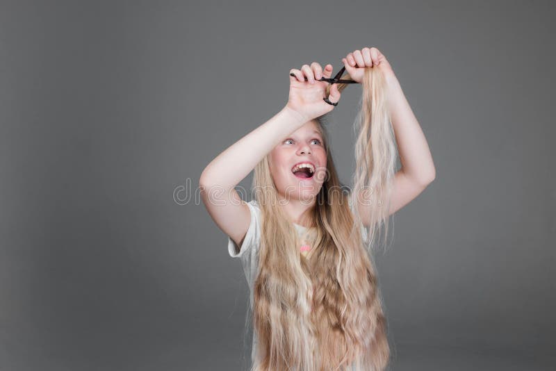 La muchacha atractiva del chaild está cortando su pelo natural rubio largo fotografía de archivo La muchacha atractiva del chaild está cortando su pelo natural rubio largo fotografía de archivo