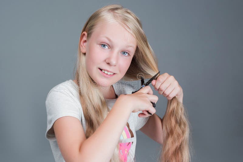 La muchacha atractiva del chaild está cortando su pelo natural rubio largo imagen de archivo La muchacha atractiva del chaild está cortando su pelo natural rubio largo imagen de archivo