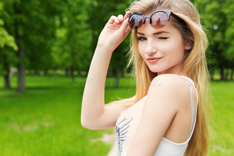 La muchacha atractiva feliz linda hermosa con el pelo largo rubio en la camiseta blanca levantó las gafas de sol y guiñó imagenes de archivo La muchacha atractiva feliz linda hermosa con el pelo largo rubio en la camiseta blanca levantó las gafas de sol y guiñó imagenes de archivo