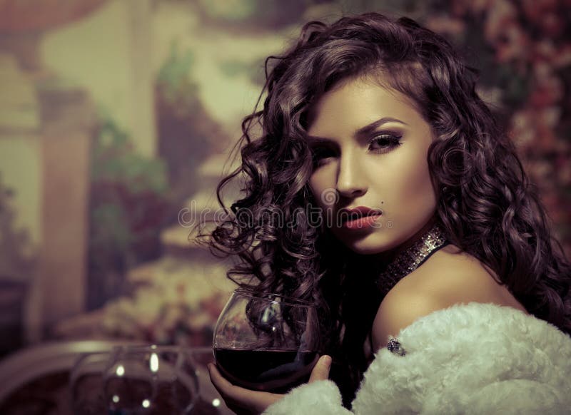 La muchacha atractiva se sienta con el vino en abrigo de pieles en la tarde imagen de archivo libre de regalías La muchacha atractiva se sienta con el vino en abrigo de pieles en la tarde imagen de archivo libre de regalías