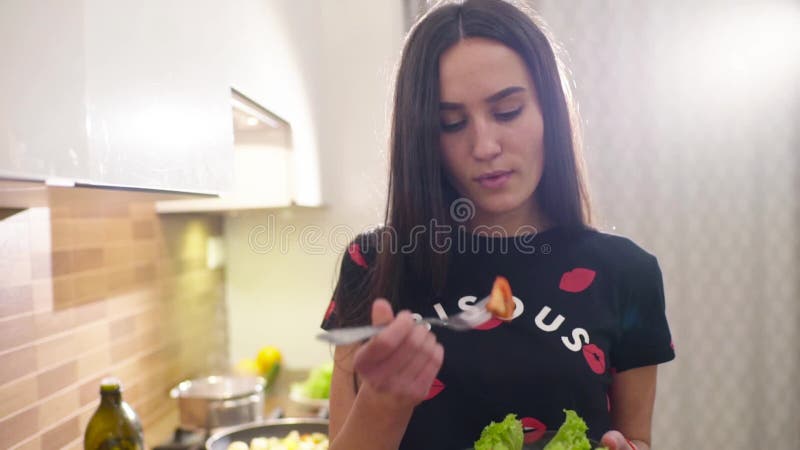 La muchacha bonita joven acaba de cocinar una ensalada fresca de la lechuga y de los tomates verdes Ella goza del gusto de la com metrajes