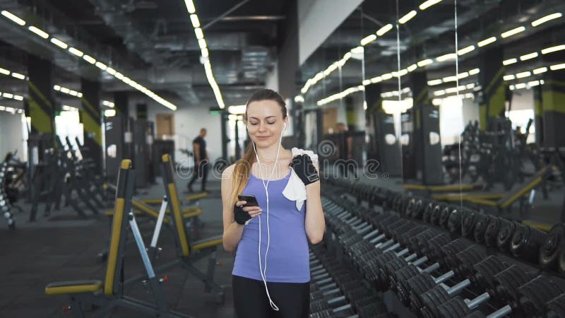 La muchacha camina con el teléfono en el gimnasio