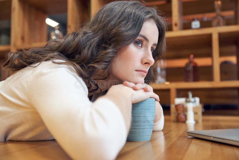 La muchacha de pelo largo joven atractiva con una cara agujereada doblada a la tabla en café y mira cuidadosamente en la distanci fotos de archivo La muchacha de pelo largo joven atractiva con una cara agujereada doblada a la tabla en café y mira cuidadosamente en la distanci fotos de archivo