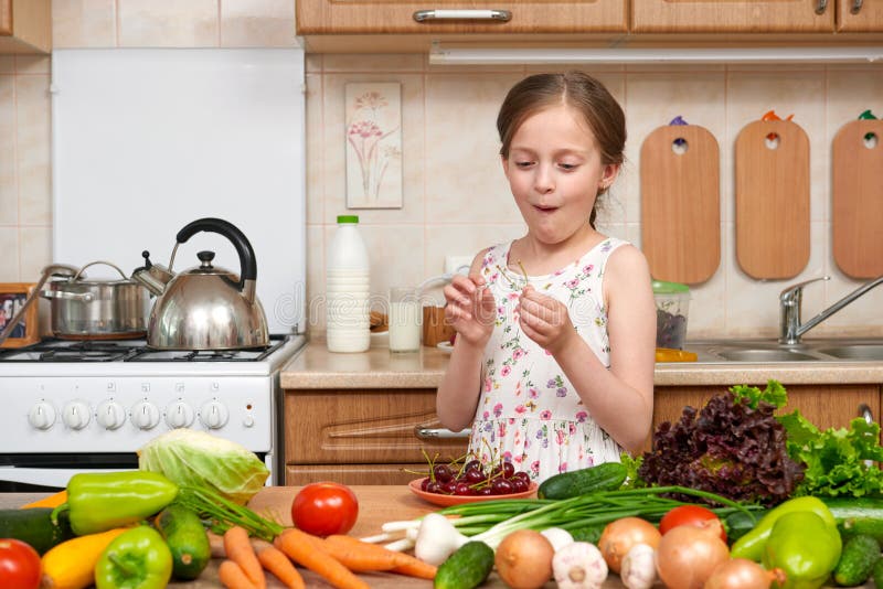 La muchacha del niño come las cerezas, frutas y verduras en la cocina casera interior, concepto sano de la comida imagen de archivo La muchacha del niño come las cerezas, frutas y verduras en la cocina casera interior, concepto sano de la comida imagen de archivo