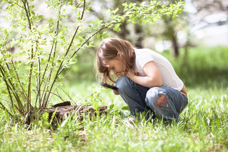 Kid girl with magnifying glass explores the grass and stump, childhood, and knowledge of the world. Kid girl with magnifying glass explores the grass and stump, childhood, and knowledge of the world