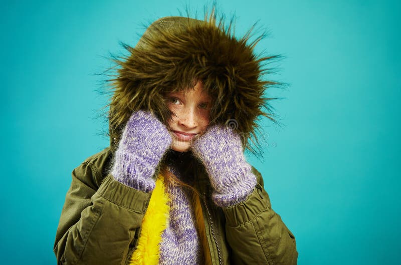 La muchacha del niño en chaqueta caliente del otoño con la capilla de la piel en verde y las manoplas, tiro en azul aisló el fond fotos de archivo La muchacha del niño en chaqueta caliente del otoño con la capilla de la piel en verde y las manoplas, tiro en azul aisló el fond fotos de archivo
