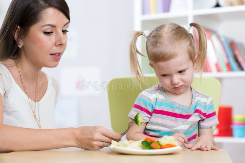 La muchacha del niño mira con repugnancia las verduras sanas La madre convence a su hija comer la comida foto de archivo libre de regalías La muchacha del niño mira con repugnancia las verduras sanas La madre convence a su hija comer la comida foto de archivo libre de regalías