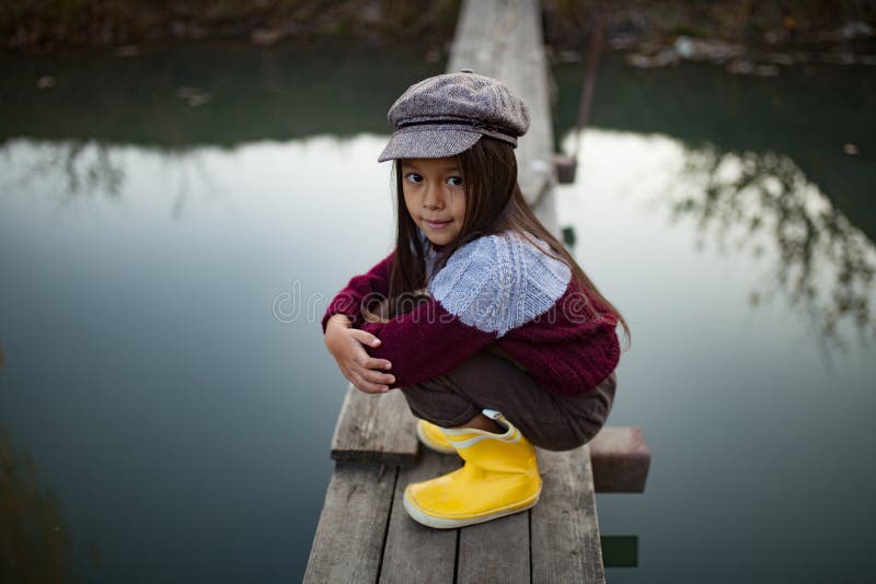 La muchacha del niño se sienta en el puente de madera en el fondo del río fotografía de archivo La muchacha del niño se sienta en el puente de madera en el fondo del río fotografía de archivo