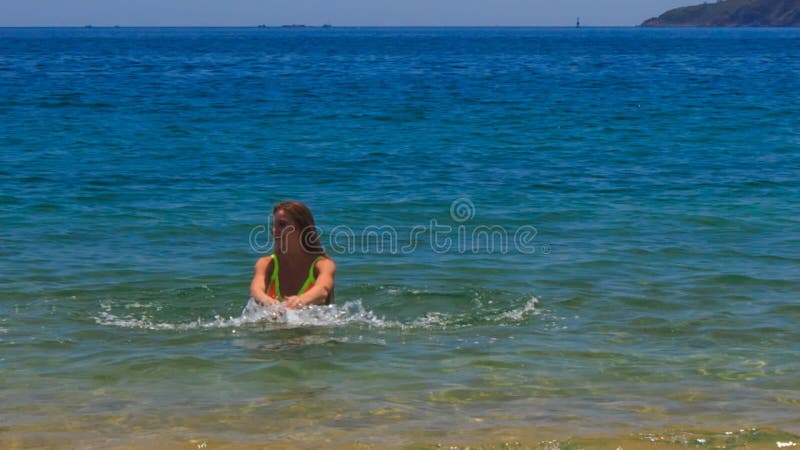 la muchacha delgada rubia en funcionamientos de la opinión de la parte trasera del bikini en el agua balancea