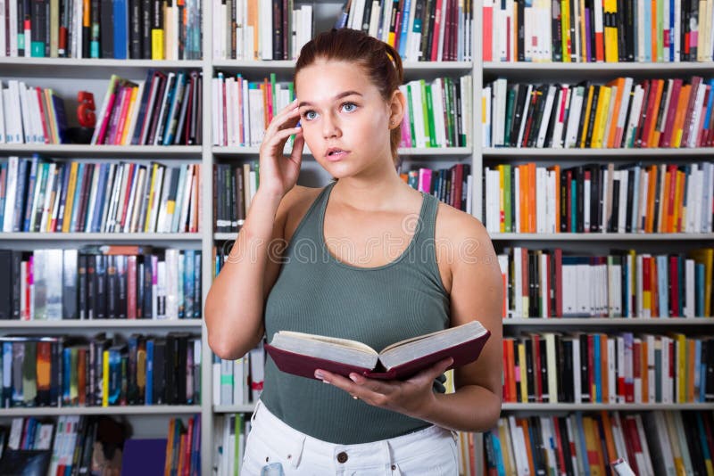 La muchacha elige un libro en la biblioteca foto de archivo libre de regalías La muchacha elige un libro en la biblioteca foto de archivo libre de regalías