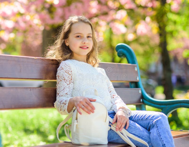 La muchacha en cara sonriente se sienta en el banco, árbol de Sakura en el fondo, defocused Concepto de los accesorios Niño lindo imagen de archivo libre de regalías La muchacha en cara sonriente se sienta en el banco, árbol de Sakura en el fondo, defocused Concepto de los accesorios Niño lindo imagen de archivo libre de regalías