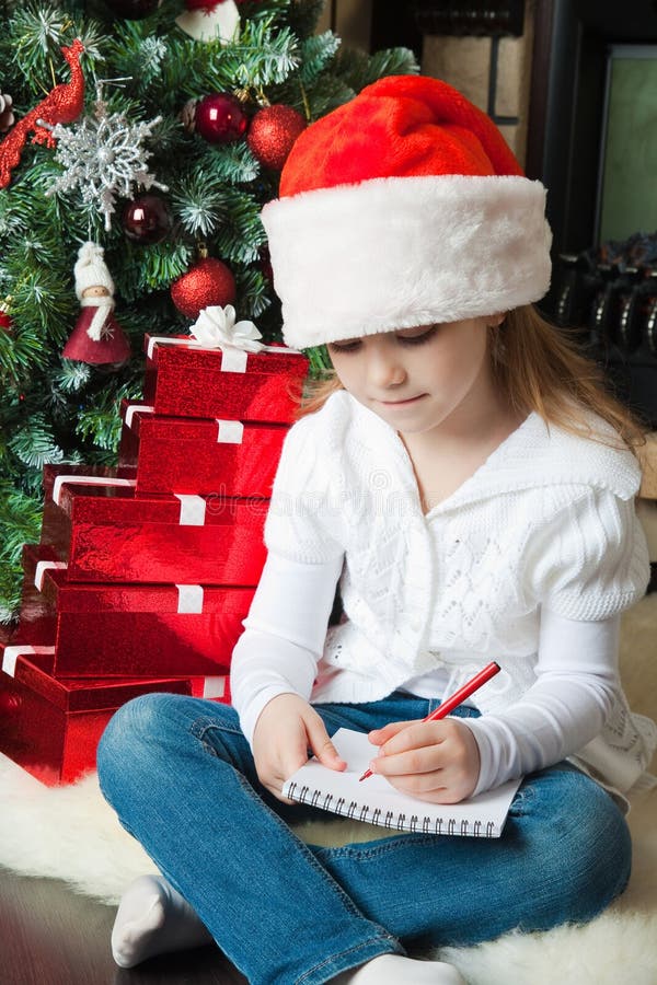 La muchacha en el sombrero de Papá Noel sienta y escribe la letra a Papá Noel imágenes de archivo libres de regalías La muchacha en el sombrero de Papá Noel sienta y escribe la letra a Papá Noel imágenes de archivo libres de regalías
