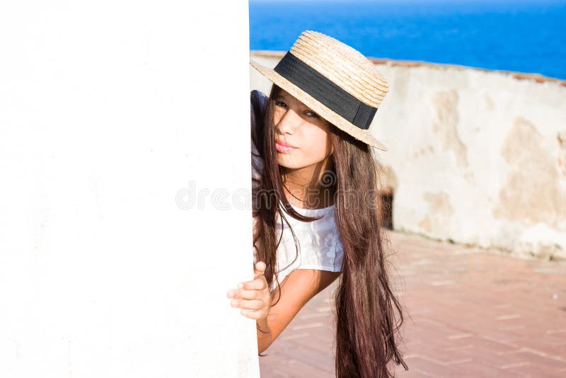 La muchacha en sombrero de paja mira a escondidas hacia fuera de detrás la pared imagen de archivo La muchacha en sombrero de paja mira a escondidas hacia fuera de detrás la pared imagen de archivo
