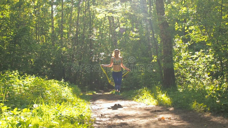 La muchacha es cuerda de salto en el parque Chica joven que hace deportes en el bosque