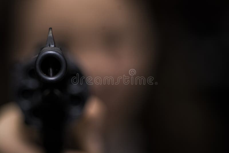 The girl is aiming from the revolver right into the photographer. focus on the muzzle of the revolver. the girl`s face is blurry. The girl is aiming from the revolver right into the photographer. focus on the muzzle of the revolver. the girl`s face is blurry