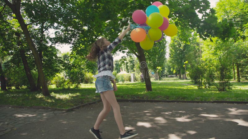La muchacha feliz, juguetona presenta con los globos coloridos en el paseo en parque soleado almacen de metraje de vídeo