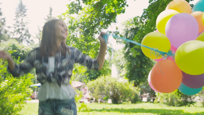 La muchacha feliz, juguetona presenta con los globos coloridos en el paseo en parque soleado almacen de video
