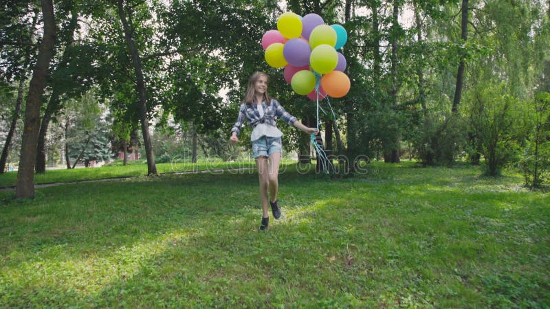 La muchacha feliz, juguetona salta con los globos coloridos en el paseo en parque soleado almacen de video