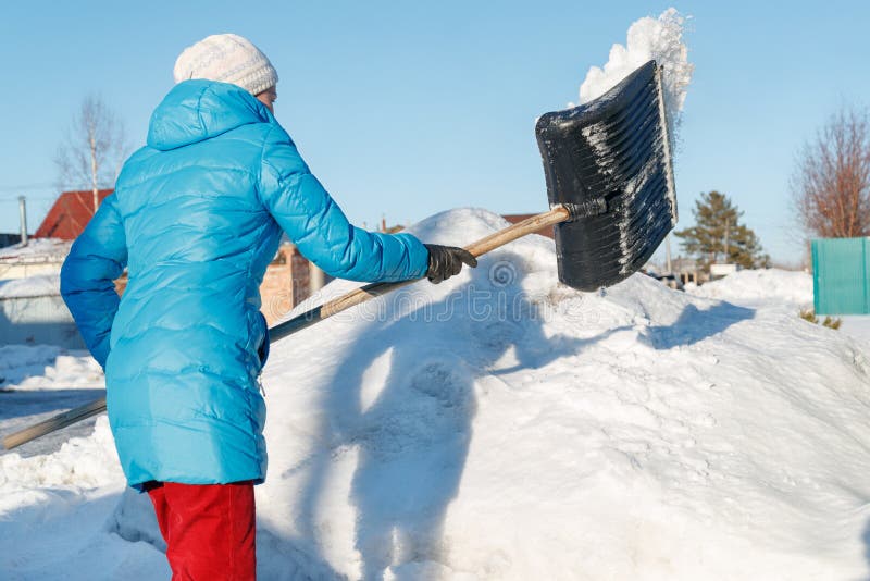 La muchacha limpia la pala de la nieve en el sitio cerca de su casa Luz del sol fotos de archivo libres de regalías La muchacha limpia la pala de la nieve en el sitio cerca de su casa Luz del sol fotos de archivo libres de regalías