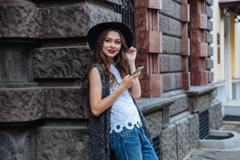 La muchacha morena hermosa sonriente de los jóvenes escucha música con los auriculares al aire libre fotografía de archivo La muchacha morena hermosa sonriente de los jóvenes escucha música con los auriculares al aire libre fotografía de archivo