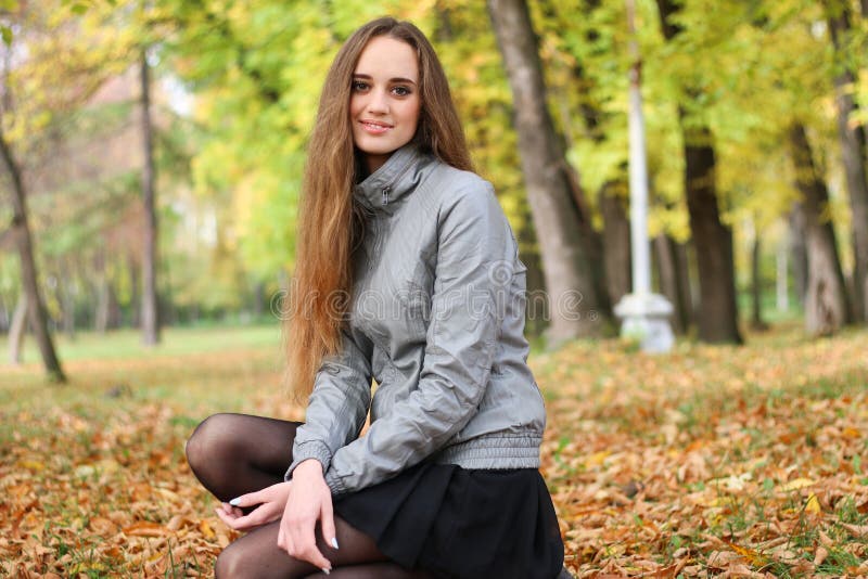 La muchacha se pone en cuclillas en madera del otoño en haces brillantes del sol foto de archivo La muchacha se pone en cuclillas en madera del otoño en haces brillantes del sol foto de archivo