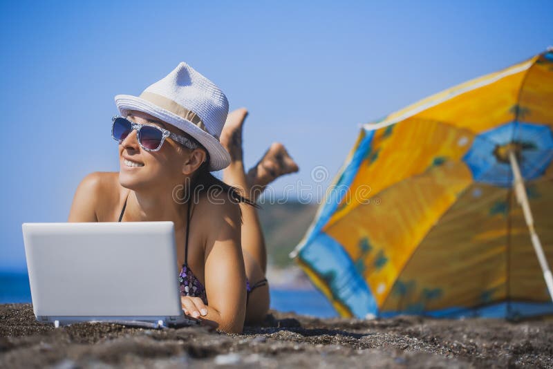 La muchacha sonriente feliz está tomando el sol con el ordenador portátil foto de archivo La muchacha sonriente feliz está tomando el sol con el ordenador portátil foto de archivo