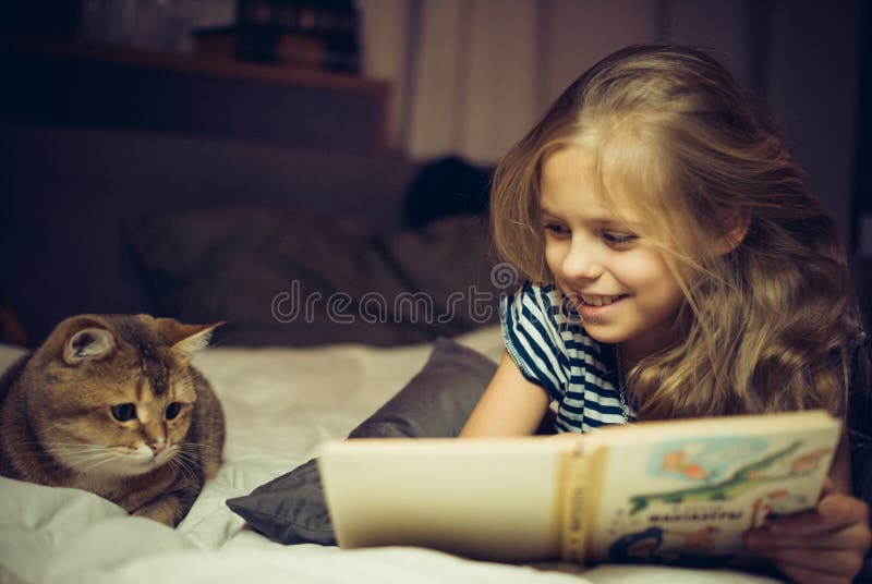 Smiling girl reads book to a cat in bed. Smiling girl reads book to a cat in bed