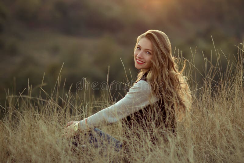 La muchacha sonriente linda con sonrisa maravillosa, linda, blanca y los labios rojos mira puesta del sol, se sienta en las colin fotografía de archivo La muchacha sonriente linda con sonrisa maravillosa, linda, blanca y los labios rojos mira puesta del sol, se sienta en las colin fotografía de archivo