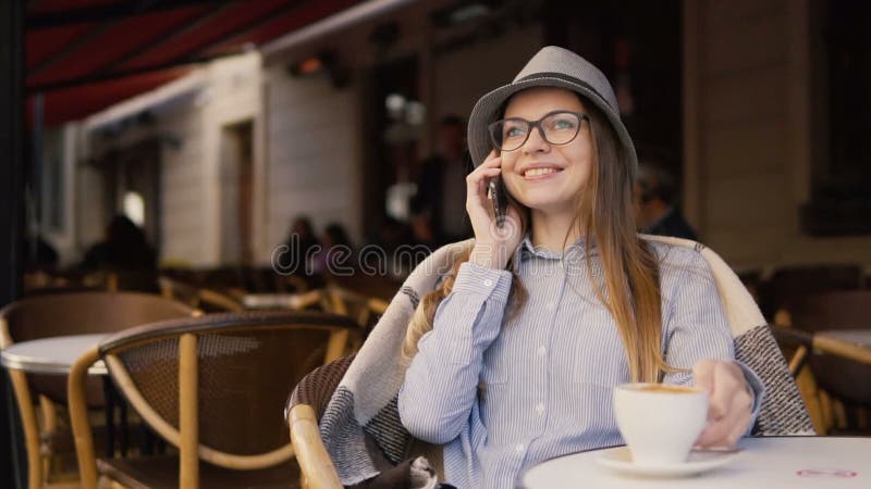 La muchacha sonriente utiliza el teléfono durante tiempo del café