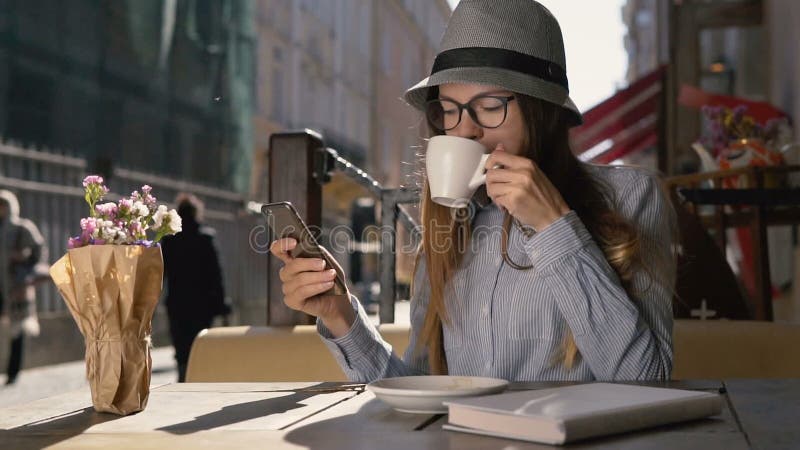 La muchacha utiliza el teléfono y goza del café