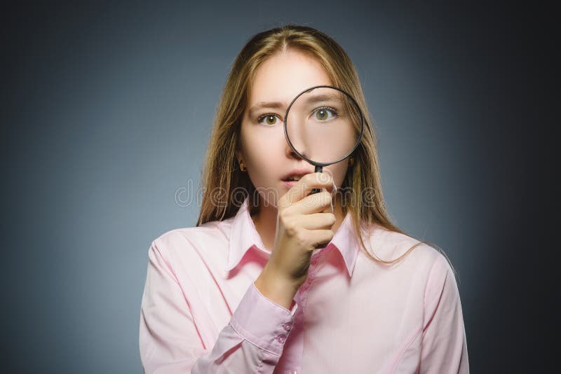 La muchacha ve a través la lupa, ojo del niño que mira con la lente de la lupa sobre gris imagen de archivo libre de regalías La muchacha ve a través la lupa, ojo del niño que mira con la lente de la lupa sobre gris imagen de archivo libre de regalías