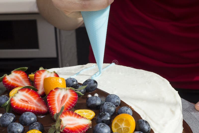 La mujer adorna una torta por la crema del dispensador fotos de archivo La mujer adorna una torta por la crema del dispensador fotos de archivo